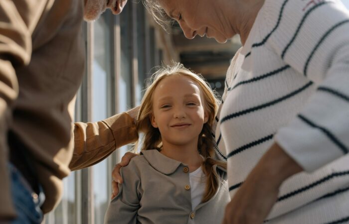 Two grandparents are holding their granddaughter that is smiling at the camera