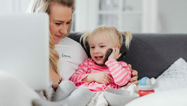 Woman holding a laptop is looking at her daughter using a mobile phone for a phone call