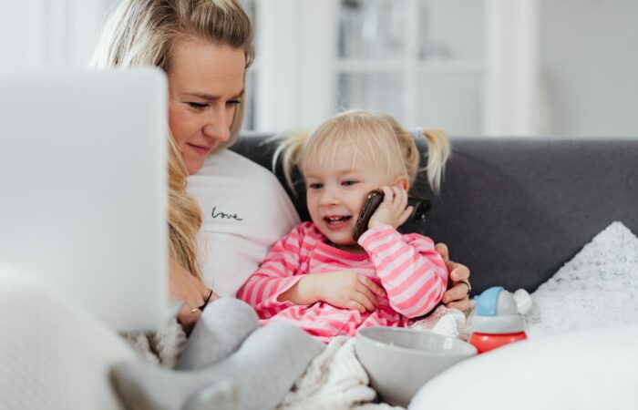 Woman holding a laptop is looking at her daughter using a mobile phone for a phone call
