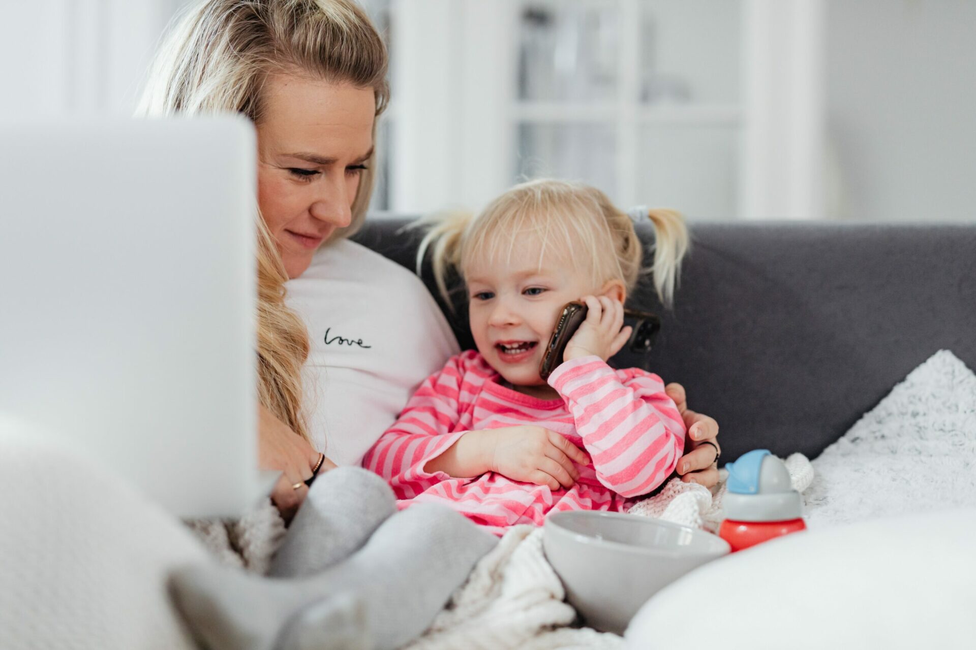 Woman holding a laptop is looking at her daughter using a mobile phone for a phone call