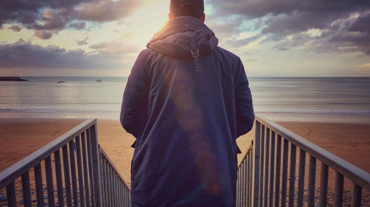Young man at the beach looking out to the sea from the top of the steps