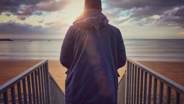 Young man at the beach looking out to the sea from the top of the steps
