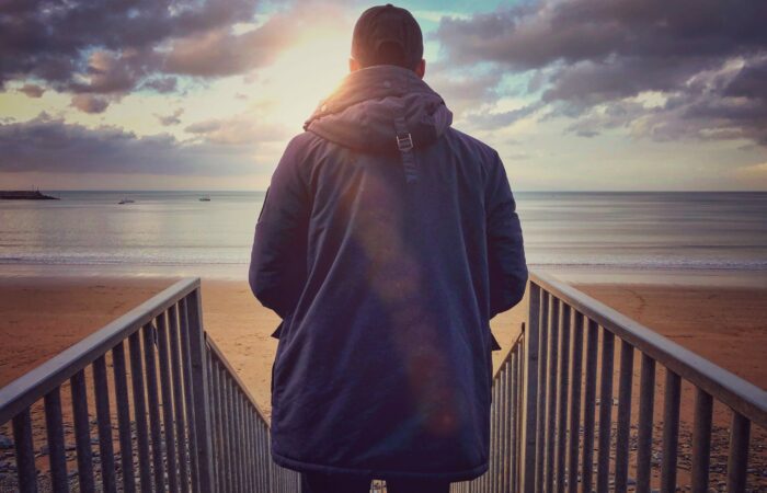Young man at the beach looking out to the sea from the top of the steps