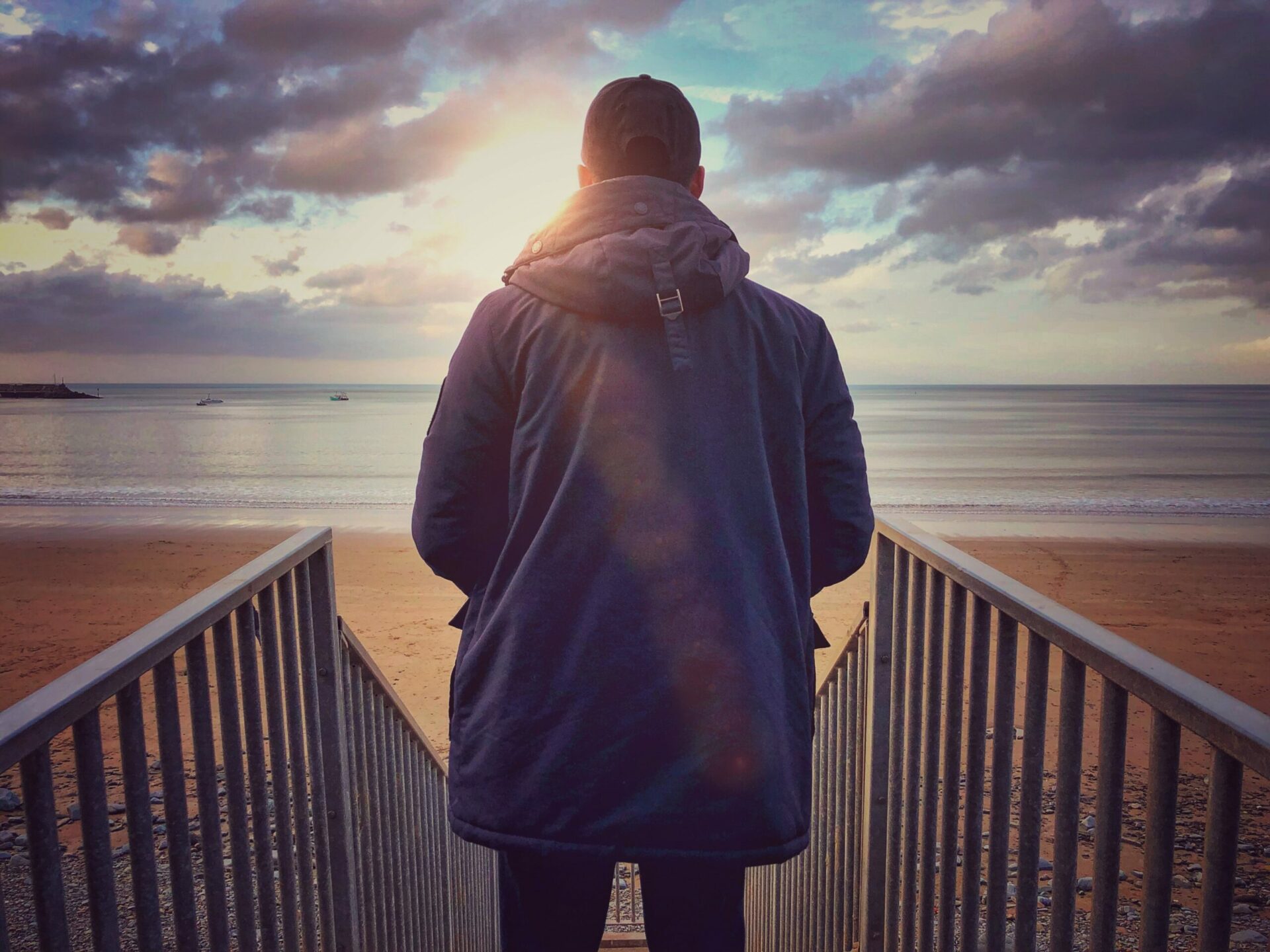 Young man at the beach looking out to the sea from the top of the steps