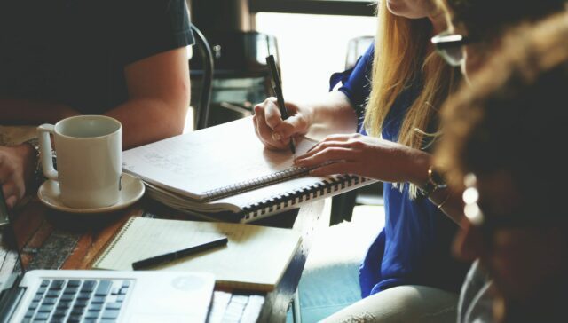 Four business people sitting at a table and one woman is writing notes on her notepad