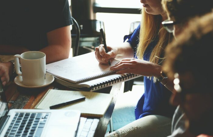 Four business people sitting at a table and one woman is writing notes on her notepad