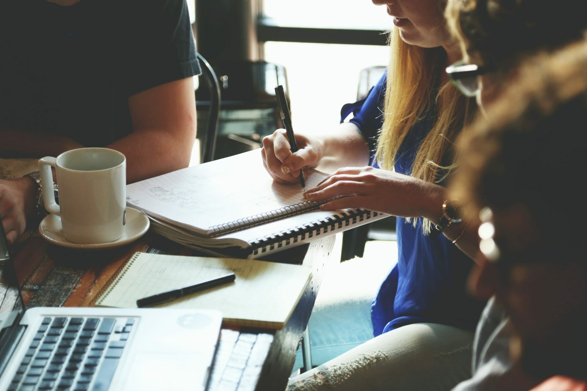 Four business people sitting at a table and one woman is writing notes on her notepad