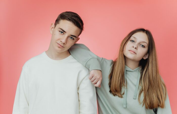 Two young people posing against a pink background.