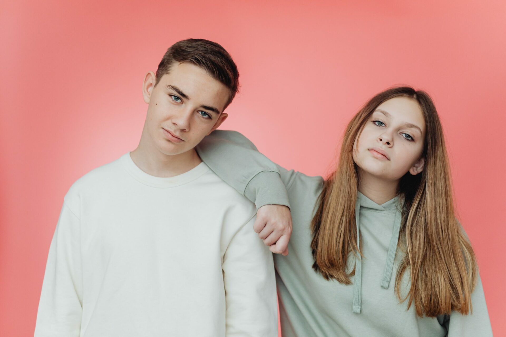 Two young people posing against a pink background.
