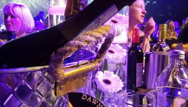 Champagne bottle lit in purple. The name 'Dawn' can be seen on a tag on a glass