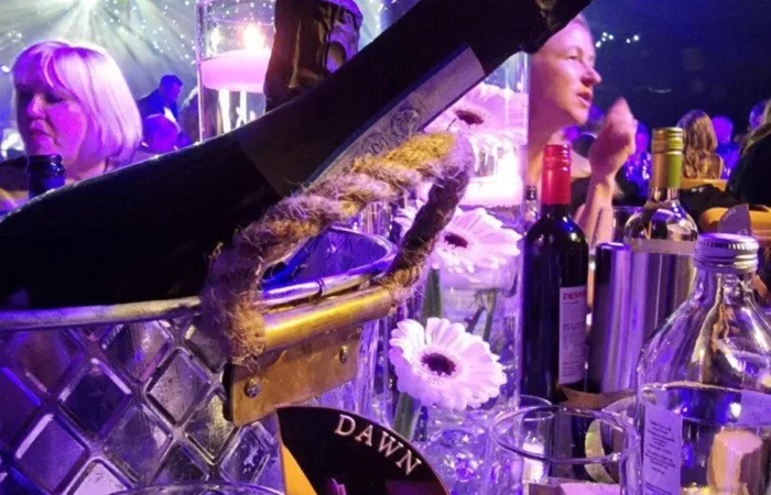 Champagne bottle lit in purple. The name 'Dawn' can be seen on a tag on a glass