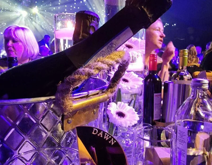 Champagne bottle lit in purple. The name 'Dawn' can be seen on a tag on a glass