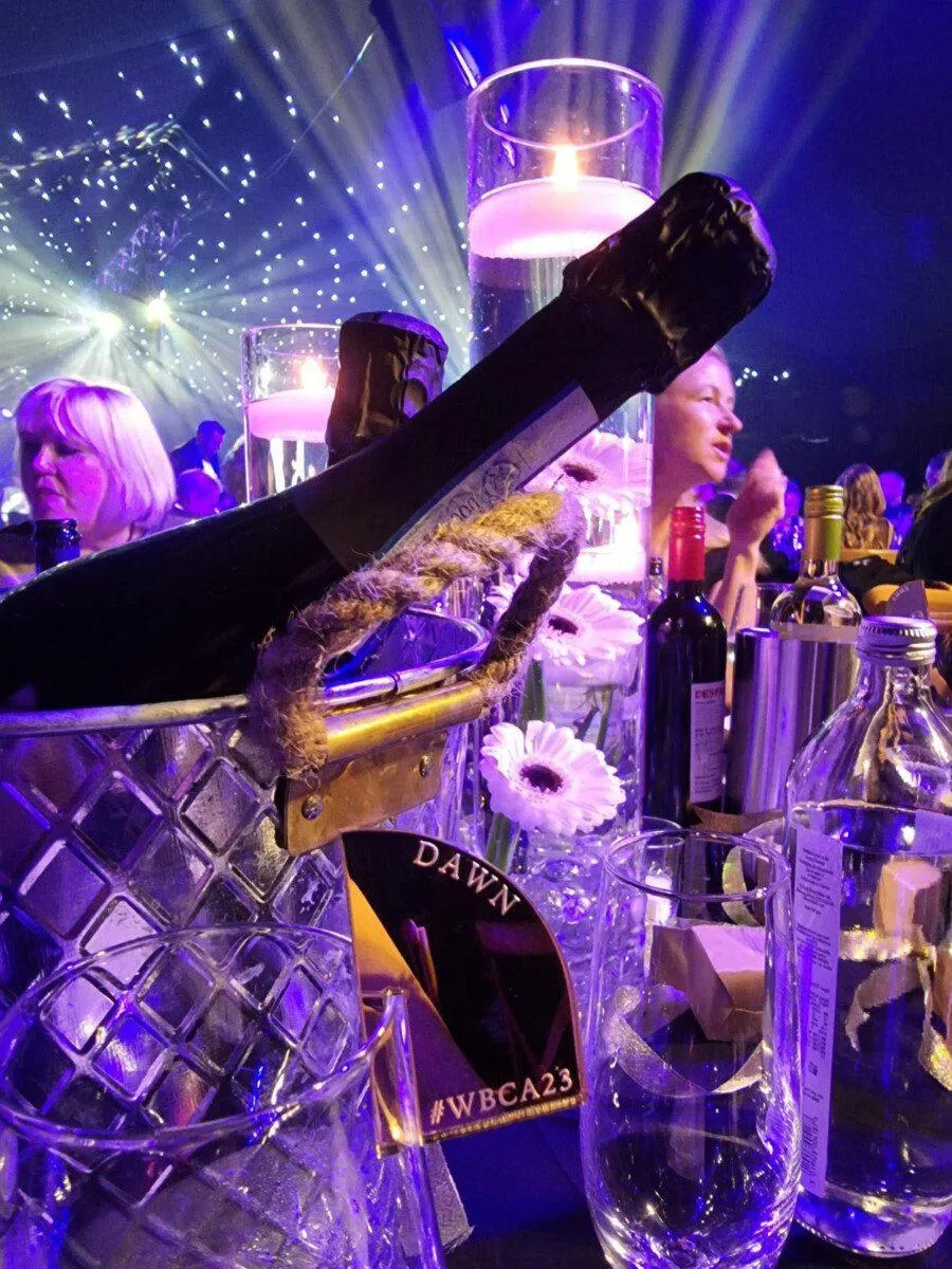 WrexhamComunityAndBusinessAward2 Champagne bottle lit in purple. The name 'Dawn' can be seen on a tag on a glass