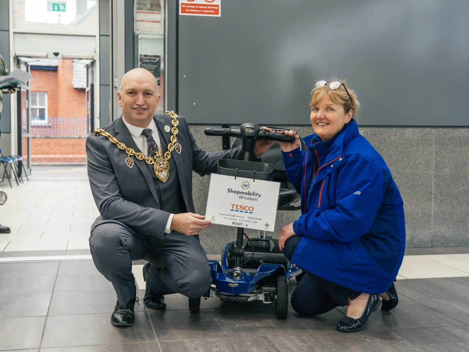 BJC04963 Two smiling people crouched near a mobility boot scooter. The people are Cllr Andy Williams, and Alison Roberts